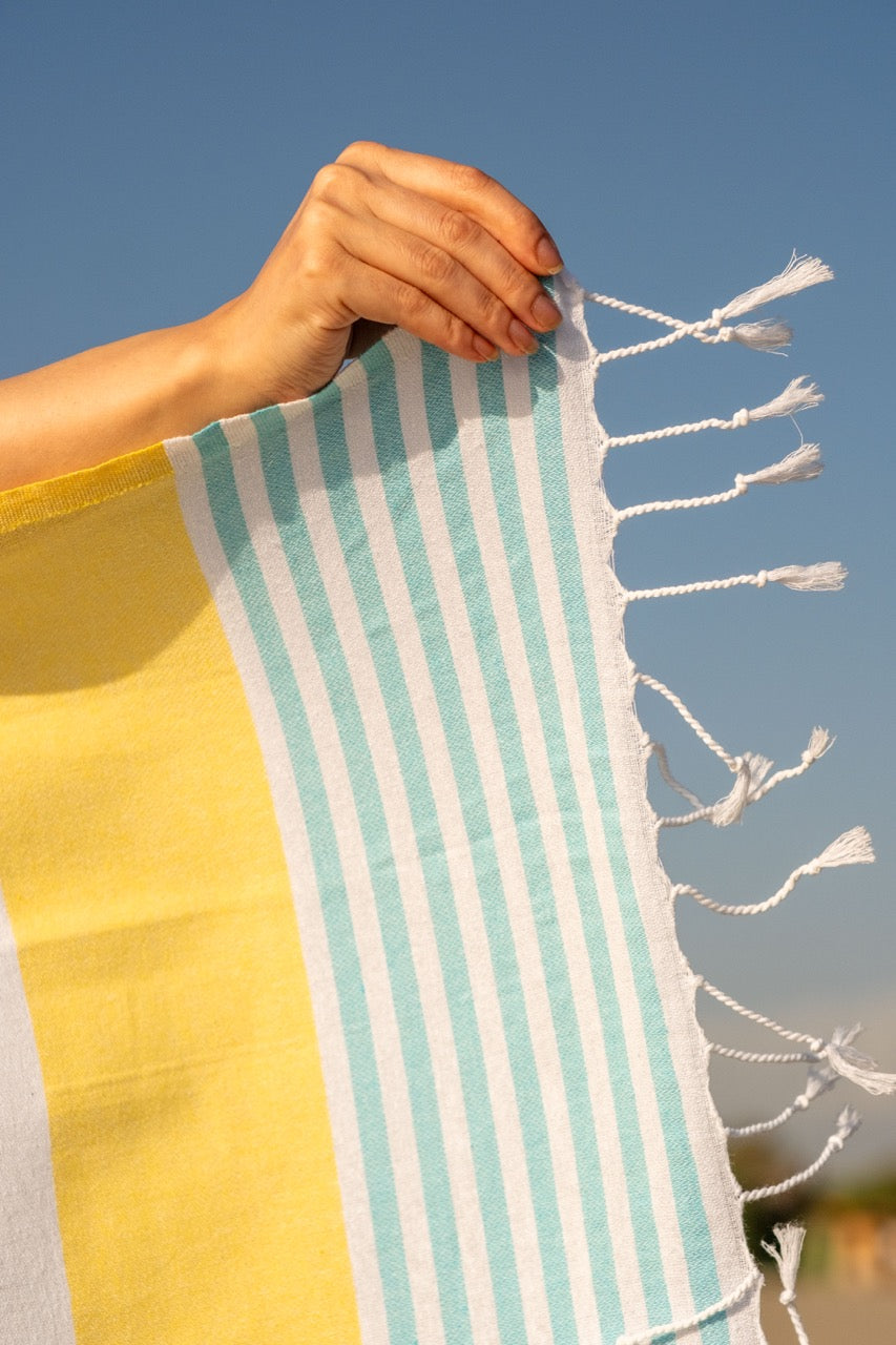 womens hand holding towel, blue sky. towel is yellow with green stripes on ends
